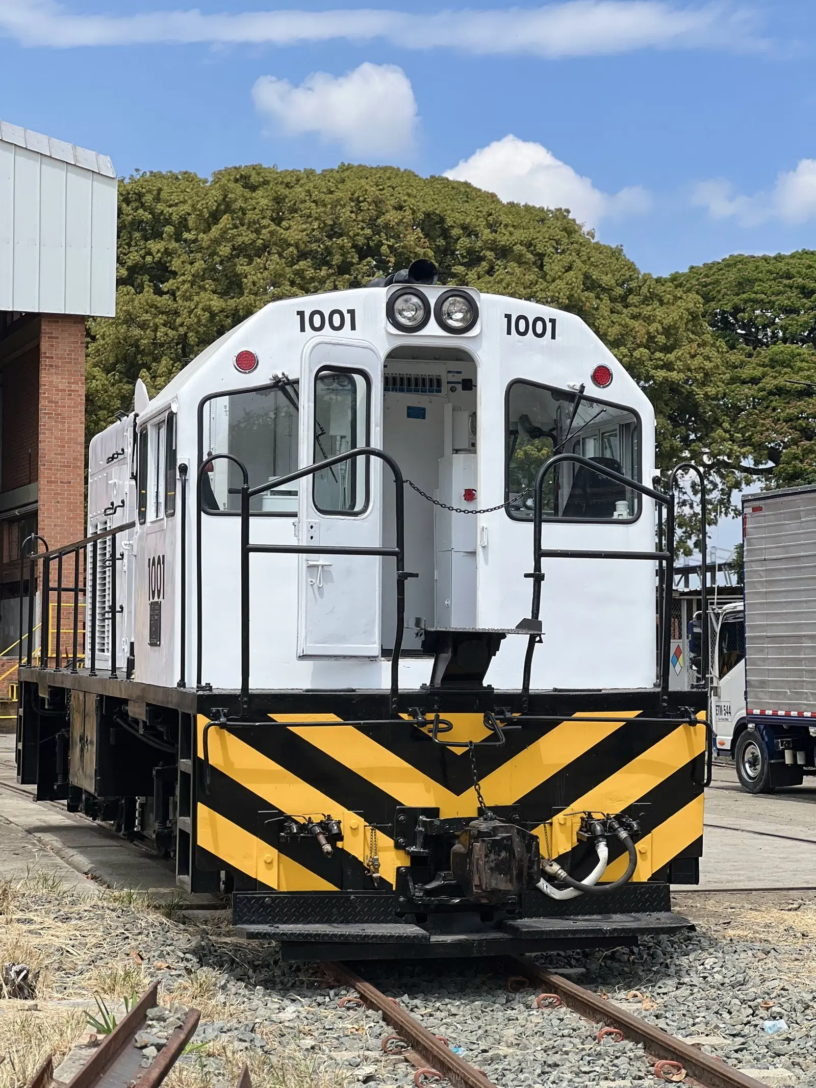 Locomotora 1001, blanca con franjas amarillas y negras, en un patio ferroviario